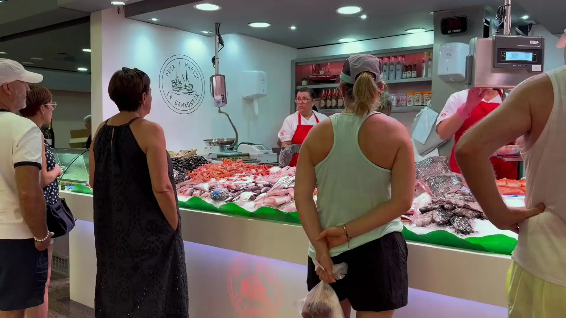 Les mans d'una peixatera de La Ganxoneta filetejant un peix sobre la fusta, amb una muntanya d'escamarlans al davant.